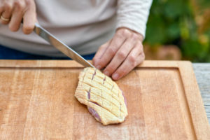 Frauenhände mit Kochmesser ritzen die Haut einer Entenbrustein, Holzbrett Frauenhände mit Kochmesser ritzen die Haut einer Entenbrustein, Holzbrett